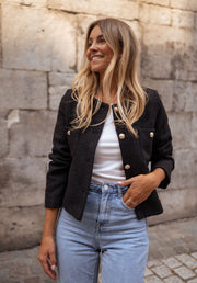 Veste droite à épaulettes portée par une femme, vue de trois-quarts, jean clair, mur en pierre