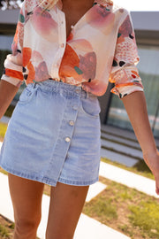 Jupe-short en jean porté par une femme, vue rapprochée, boutons, chemisier orange