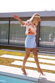 Jupe-short en jean porté par une femme, en marchant, dalles, bras écartés