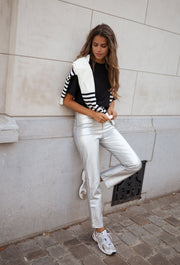 Pantalon effet cuir taille haute porté par une femme, vue de face, mur blanc, pull rayé sur les épaules