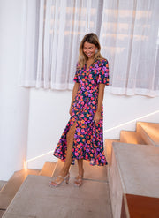 Robe longue cache-cœur fleurie portée par une femme, vue de face, escalier, rideaux