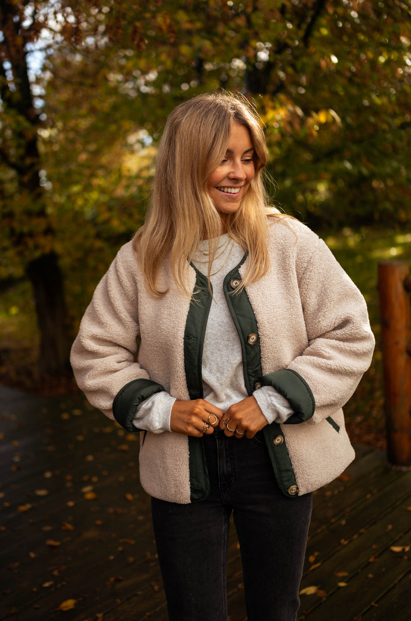 Manteau mouton effet matelassé porté par une femme, vue rapprochée, bordures vertes, mains dans les poches