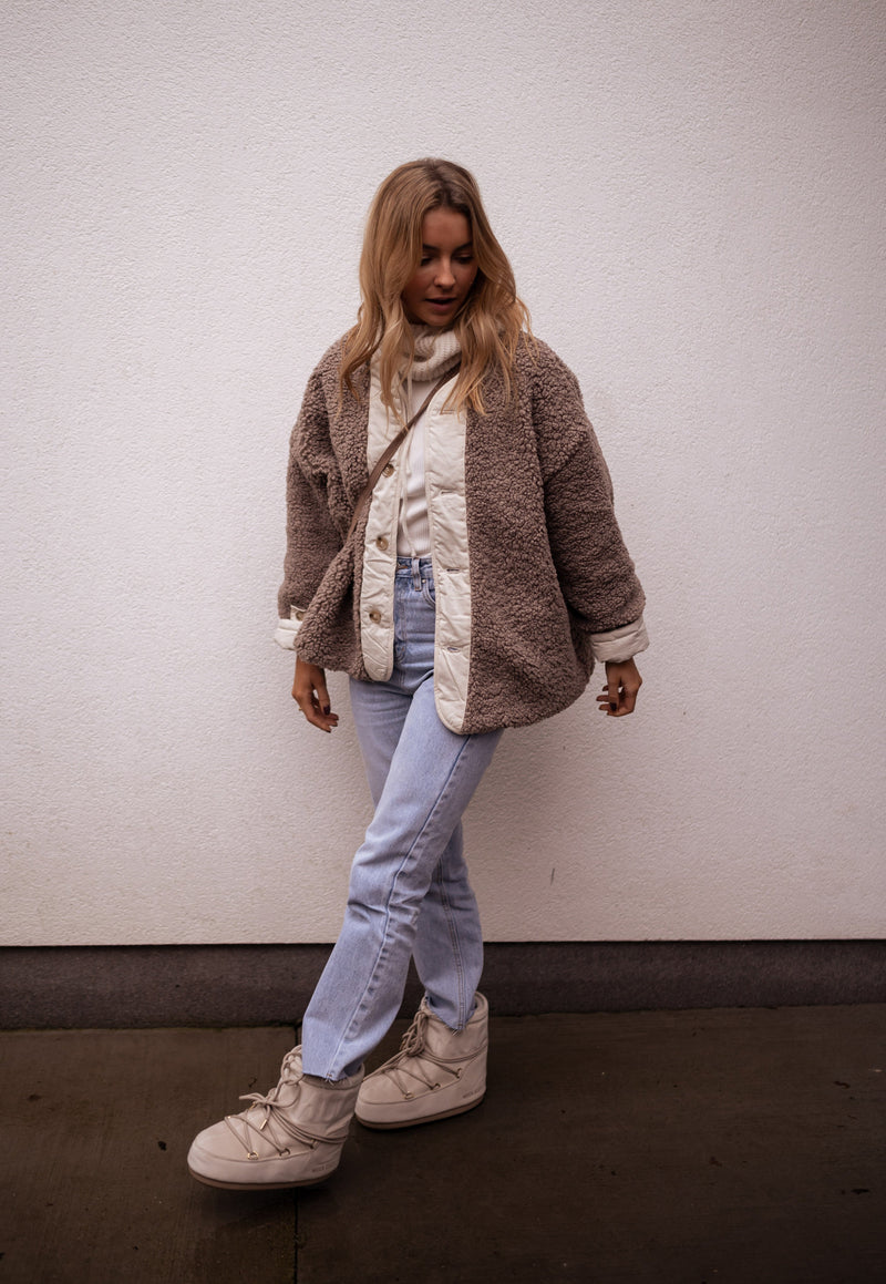 Manteau réversible effet mouton porté par une femme, vue de trois-quarts, côté marron, mur blanc, baskets blanches