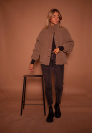 Manteau mouton à col montant porté par une femme, silhouette entière, tabouret noir, jean noir, bottines