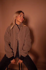 Manteau mouton à col montant porté par une femme, assise, sur un tabouret, regard vers le haut