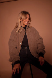 Manteau mouton à col montant porté par une femme, assise, sur un tabouret, jambes écartées