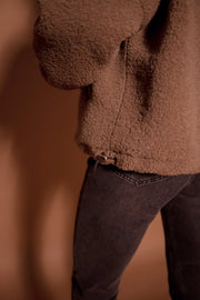 Manteau mouton à col montant porté par une femme, gros plan de la boucle et du jean noir