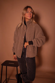 Manteau mouton à col montant porté par une femme, vue de trois-quarts, appuyée à un tabouret