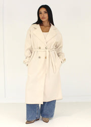 Manteau beige à boutons dorés — vue de face, ceinture nouée.