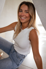 Top pailleté à col montant porté par une femme, assise, jean, sourire