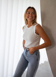 Top pailleté à col montant porté par une femme, vue de trois-quarts, rideau blanc, jean