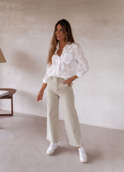 Chemise brodée à manches longues portée par une femme, silhouette entière, pantalon beige, baskets blanches