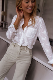 Chemise brodée à manches longues portée par une femme, vue rapprochée, main sur l'épaule, comptoir