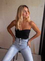 Top bustier élastiqué au dos porté par une femme, vue de trois-quarts, mur béton, jean clair