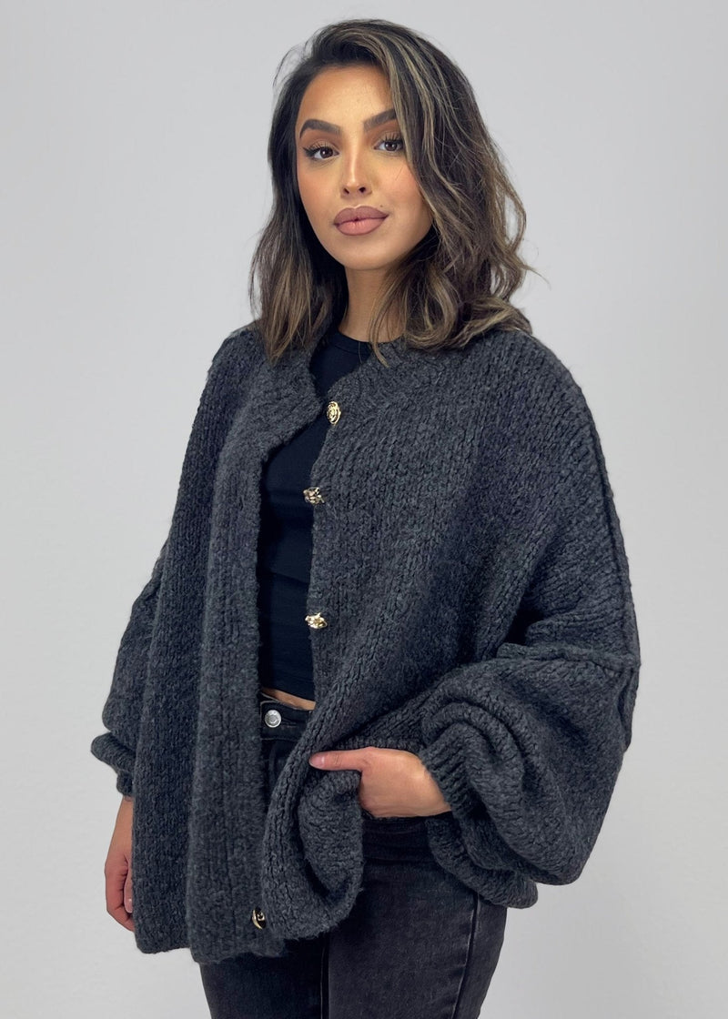 Vue rapprochée du cardigan anthracite ouvert, avec boutons dorés et manches amples.