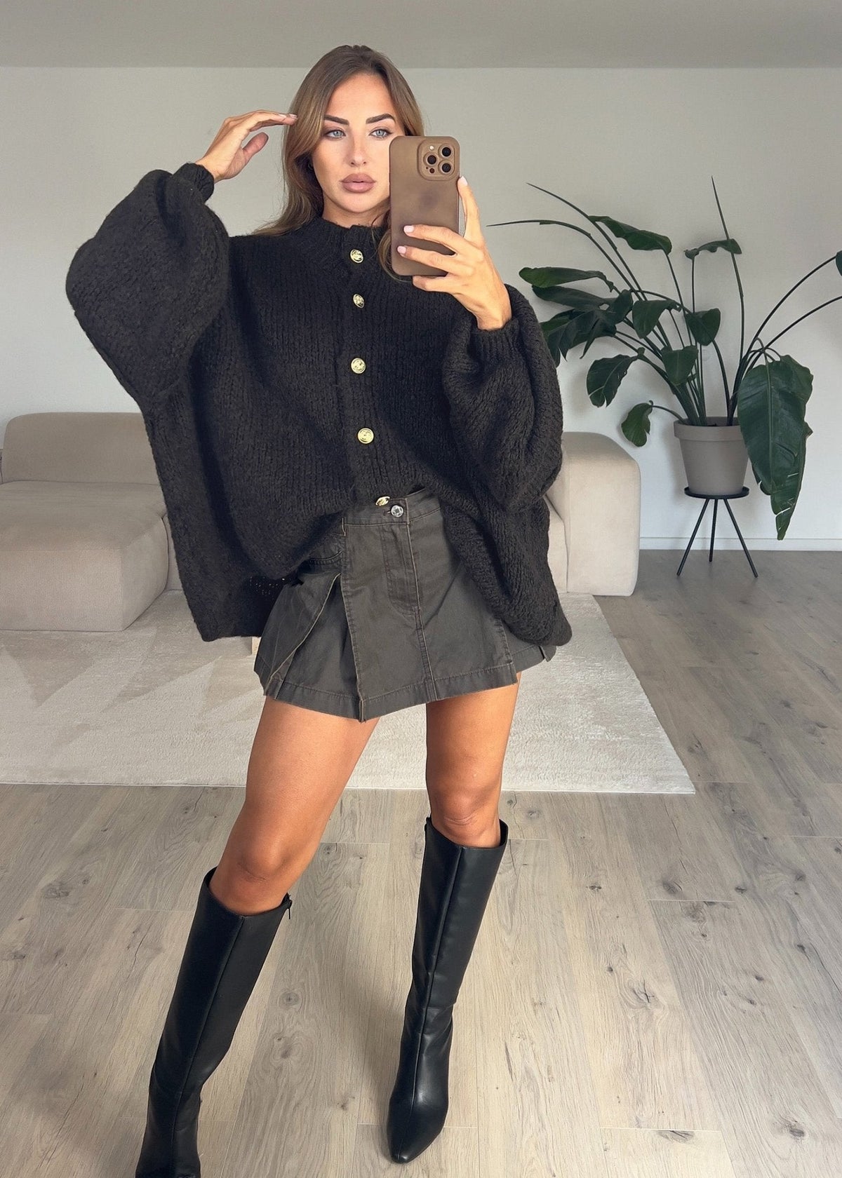 Cardigan oversize brun foncé — selfie au miroir, vue portée en pied, jupe courte grise et bottes hautes noires