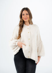 Cardigan oversize beige clair — vue portée de face, une main dans la poche du pantalon noir
