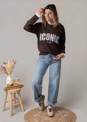 Pull en maille dentelle brodée porté par une femme, vue de trois-quarts, main sur la tête, jean large