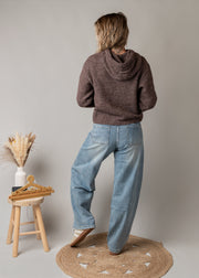 Jean coupe ballon délavé porté par une femme, vue de profil, jambe croisée, tabouret