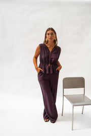 Pantalon fluide en tissu léger porté par une femme, silhouette entière, chaise grise, haut aubergine