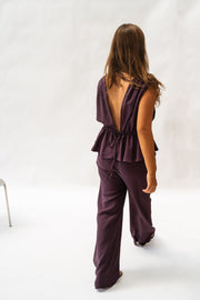 Pantalon fluide en tissu léger porté par une femme, vue de profil, haut aubergine, fond blanc