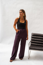 Pantalon fluide en tissu léger porté par une femme, silhouette entière, haut noir, chaise