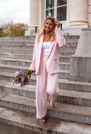 Pantalon droit fluide porté par une femme, vue de trois-quarts, blazer rose, marches