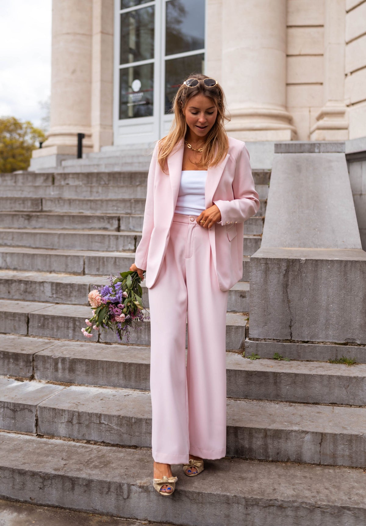Pantalon droit fluide porté par une femme, silhouette entière, marches, bouquet violet