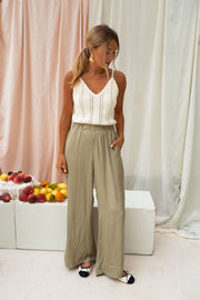 Pantalon fluide taille élastique porté par une femme, silhouette entière, rideaux, fruits, top blanc ajouré