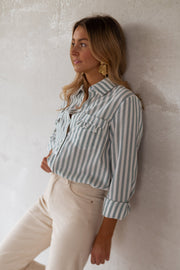 Chemise rayée à poches volantées portée par une femme, vue de profil, adossée au mur, pantalon beige