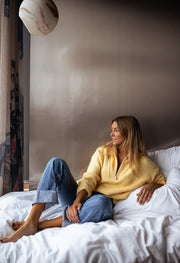 Pull loose col camionneur porté par une femme, assise, sur un lit, de loin