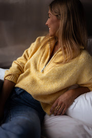 Pull loose col camionneur porté par une femme, assise, sur le lit, regard vers la fenêtre