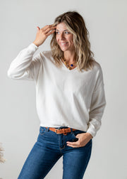 Pull fin à dos dentelle porté par une femme, vue de trois-quarts, main sur la tête, jean