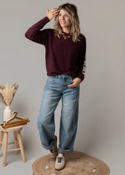 Pull à cœurs brodés porté par une femme, vue de trois-quarts, main sur la tête, jean
