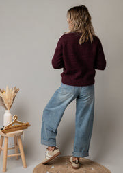 Pull à cœurs brodés porté par une femme, vue de dos, jean large, tabouret