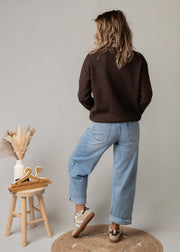 Pull en maille dentelle brodée porté par une femme, vue de dos, jean large, tabouret
