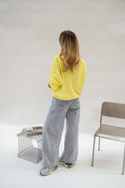 Pull effet polaire ample jaune porté par une femme, vue de dos, chaise grise, jean gris
