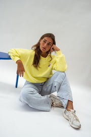 Pull effet polaire ample jaune porté par une femme, assise, tabouret bleu, baskets