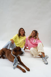Pull effet polaire ample jaune porté par une femme, assise, sol blanc, chien brun