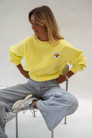 Pull effet polaire ample jaune porté par une femme, assise, tabouret métallique, baskets