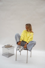 Pull effet polaire ample jaune porté par une femme, assise, tabouret métallique, jean gris