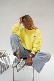 Pull effet polaire ample jaune porté par une femme, assise, tabouret, jean large