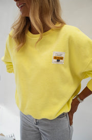 Pull effet polaire ample jaune porté par une femme, vue rapprochée, écusson, jean gris