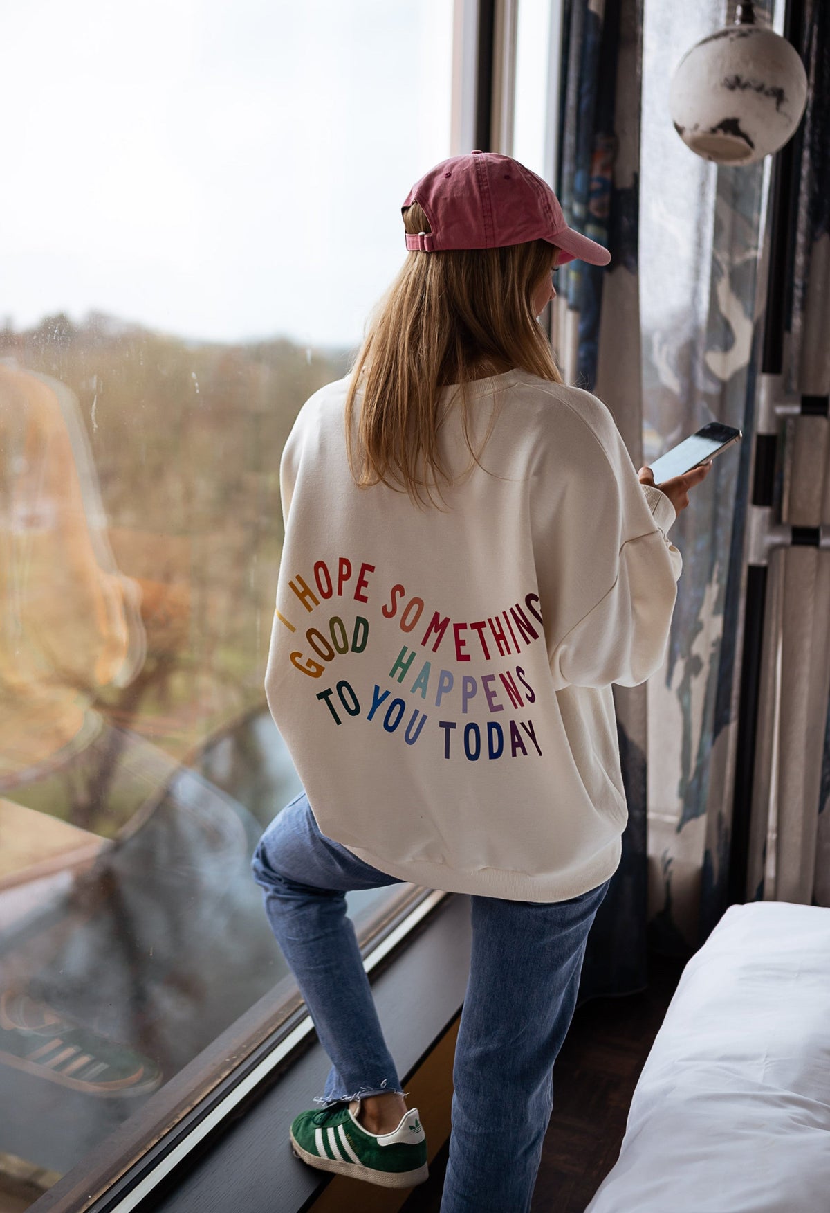 Sweat doux à écritures porté par une femme, vue de dos, inscription colorée, casquette rose, jean