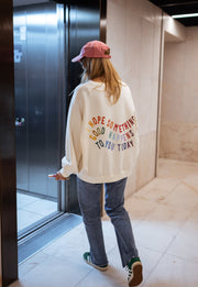 Sweat doux à écritures porté par une femme, vue de dos, casquette rose, ascenseur, baskets vertes