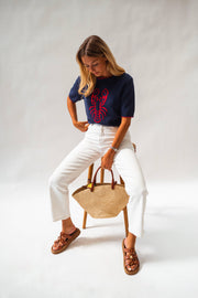 Pull en maille manches courtes porté par une femme, assise, tabouret, sac en paille