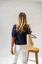 Pull en maille manches courtes porté par une femme, vue de dos, sac en paille, tabouret