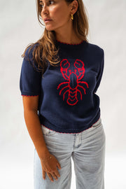 Pull en maille manches courtes porté par une femme, vue rapprochée, motif homard rouge, jean clair