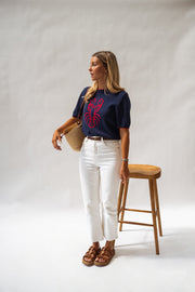 Pull en maille manches courtes porté par une femme, silhouette entière, tabouret, sac, de loin