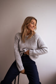 Pull dos ouvert à nœud porté par une femme, assise, sur un tabouret, jean foncé